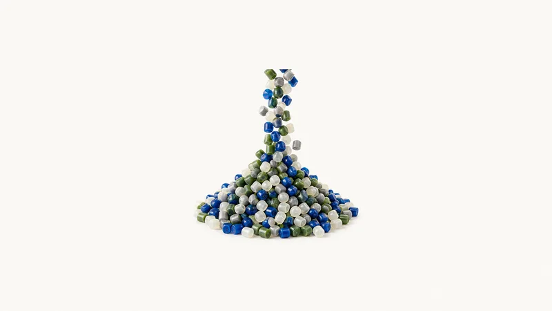 Abstract a cascade of coloured polymer pellets pooling together motif centred on a seamless pale off-white studio background, generous empty margin for overlaid branding