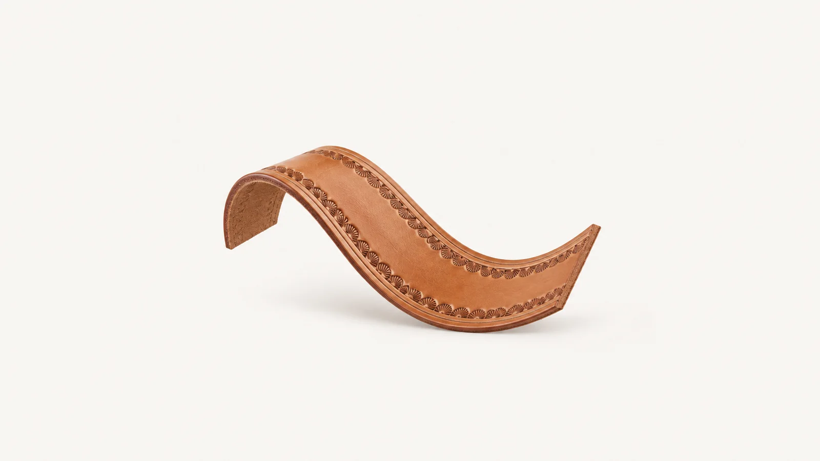 Abstract a curved sweep of tooled leather with a border stamp motif centred on a seamless pale off-white studio background, generous empty margin for overlaid branding