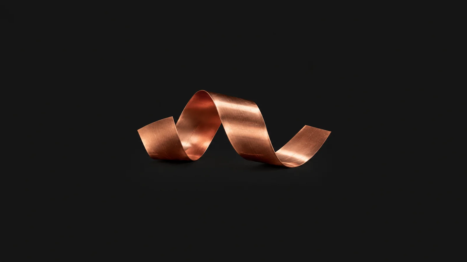 Abstract a flowing ribbon of copper foil catching amber light motif centred on a seamless deep charcoal near-black studio background, generous empty margin for overlaid branding