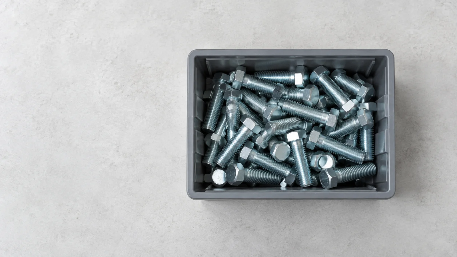Styled flat-lay of a bin of zinc-plated high-tensile hex bolts on a clean background, clean even studio light, generous negative space for overlaid text