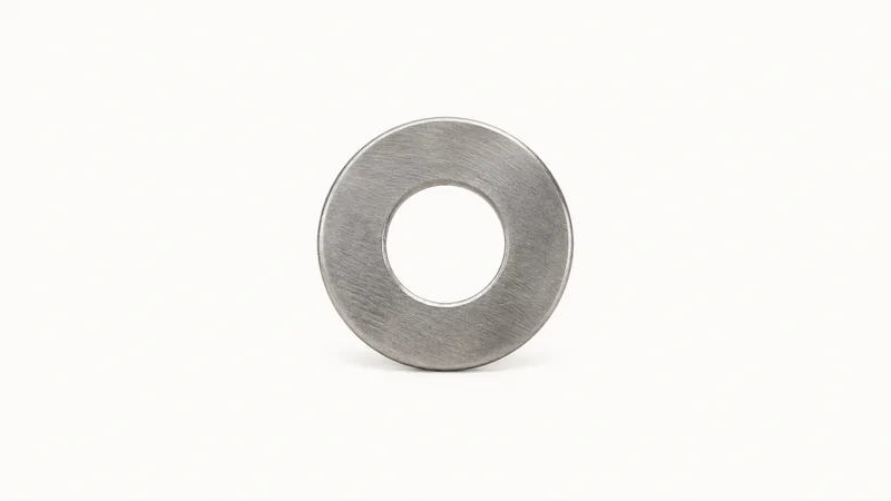 Isolated a stainless steel flat washer centred on a seamless pale off-white studio background, generous empty margin on every side for overlaid branding