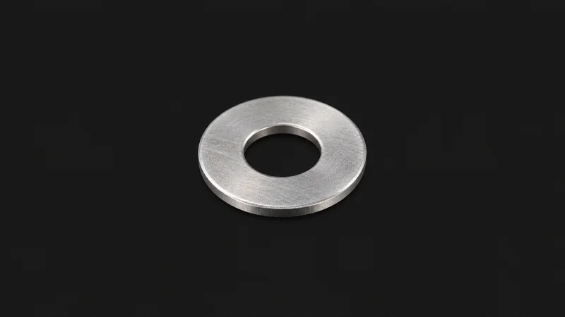 Isolated a stainless steel flat washer centred on a seamless deep charcoal near-black studio background, generous empty margin on every side for overlaid branding