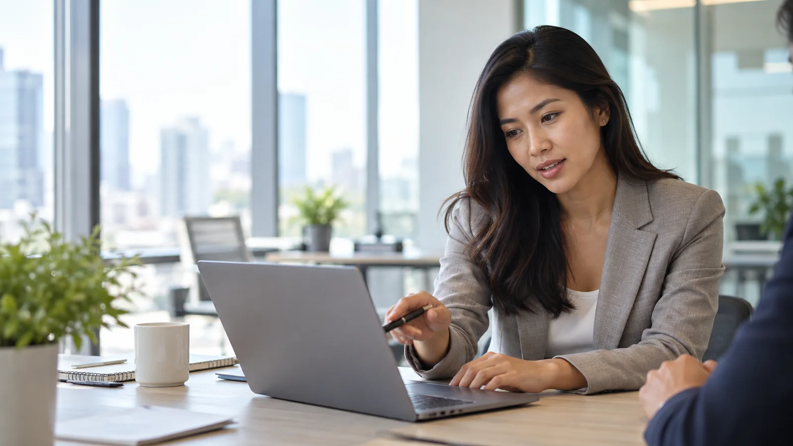 A business professional in a tailored suit collaborating around a laptop, bright daylight through the windows