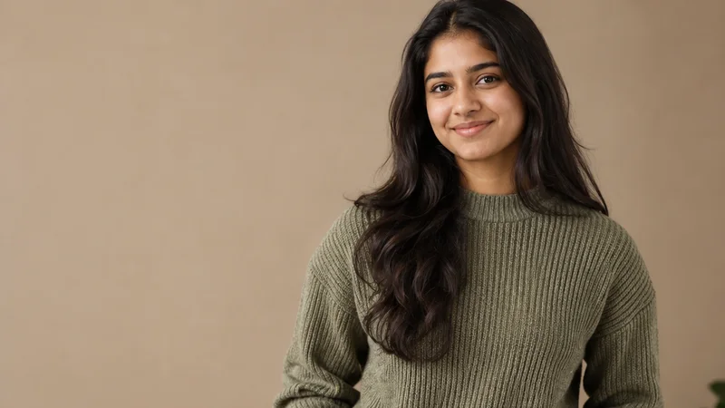 Mid-length portrait of a South Asian teenager in casual everyday clothing, professional portraits, warm interior light, plain working backdrop with copy space