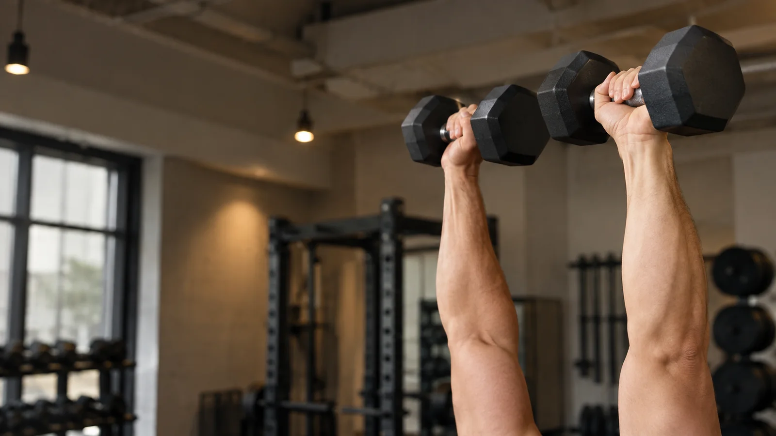 Close-up of hands demonstrating a Dumbbell Shoulder Press, warm interior light, only naturally framed hands, no faces