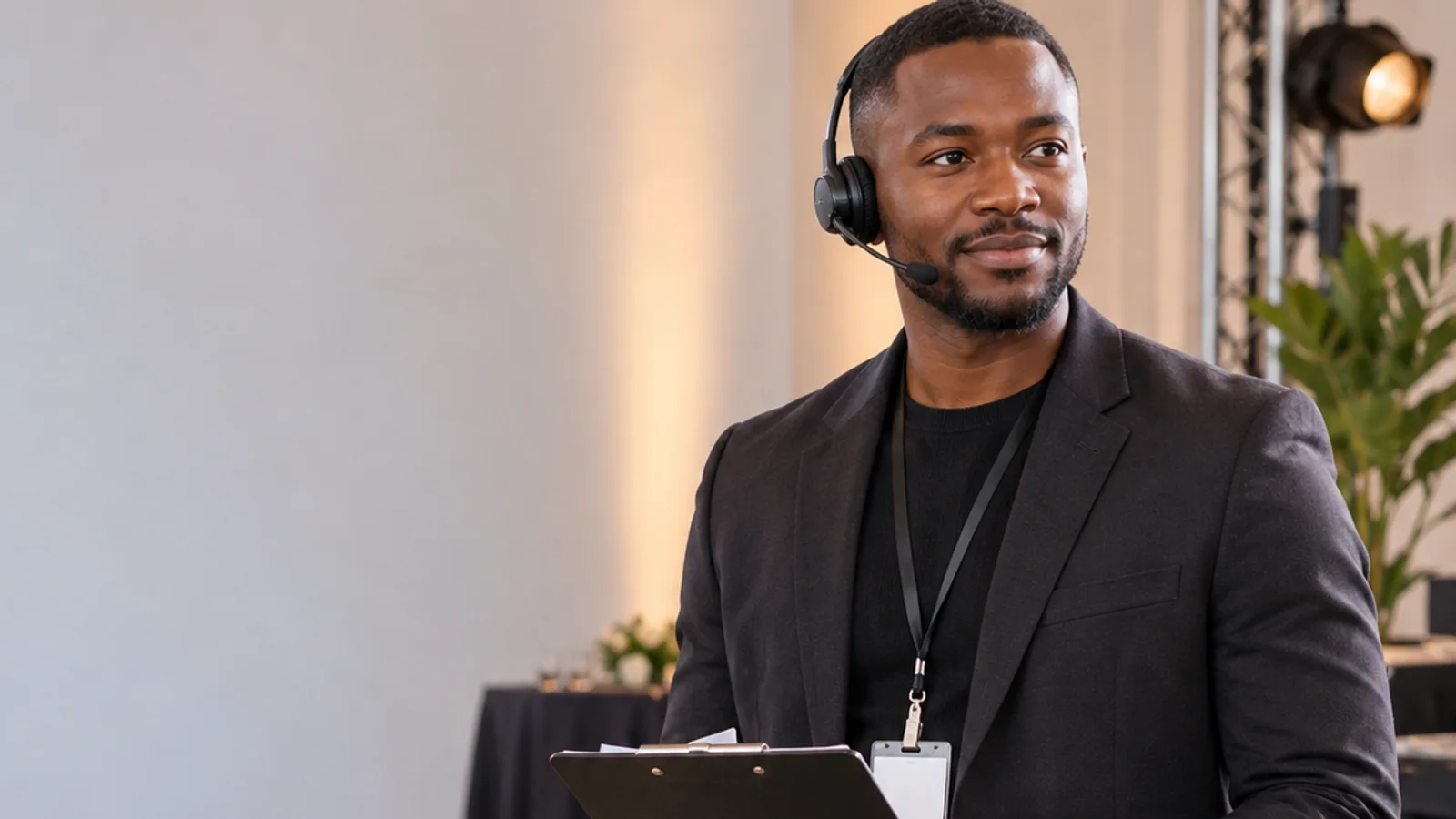 Mid-length portrait of a event coordinator with a headset and clipboard, marketing agency, warm interior light, plain working backdrop with copy space