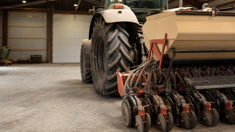 Close, clean detail of the tractor with an attached seed drill, golden-hour light, no people in frame