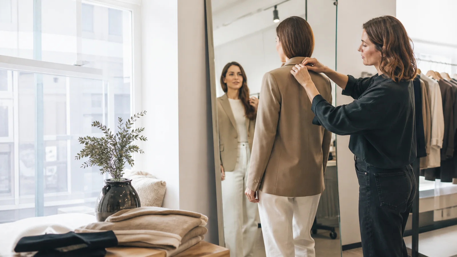 A stylist styling a customer at a fitting mirror, bright daylight through the windows