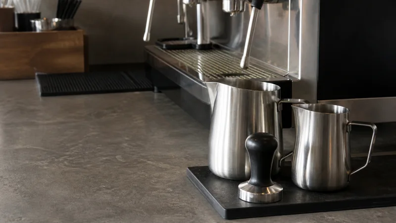 Close, clean detail of the milk steaming pitchers and tamper, soft even indoor light, no people in frame