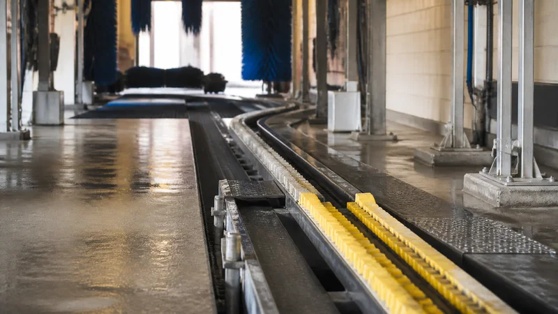 Close, clean detail of the conveyor track guiding a car through the tunnel, warm interior light, no people in frame