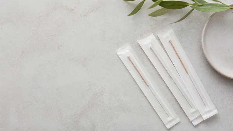 Styled flat-lay of acupuncture needles in packets on a clean background, clean even studio light, generous negative space for overlaid text