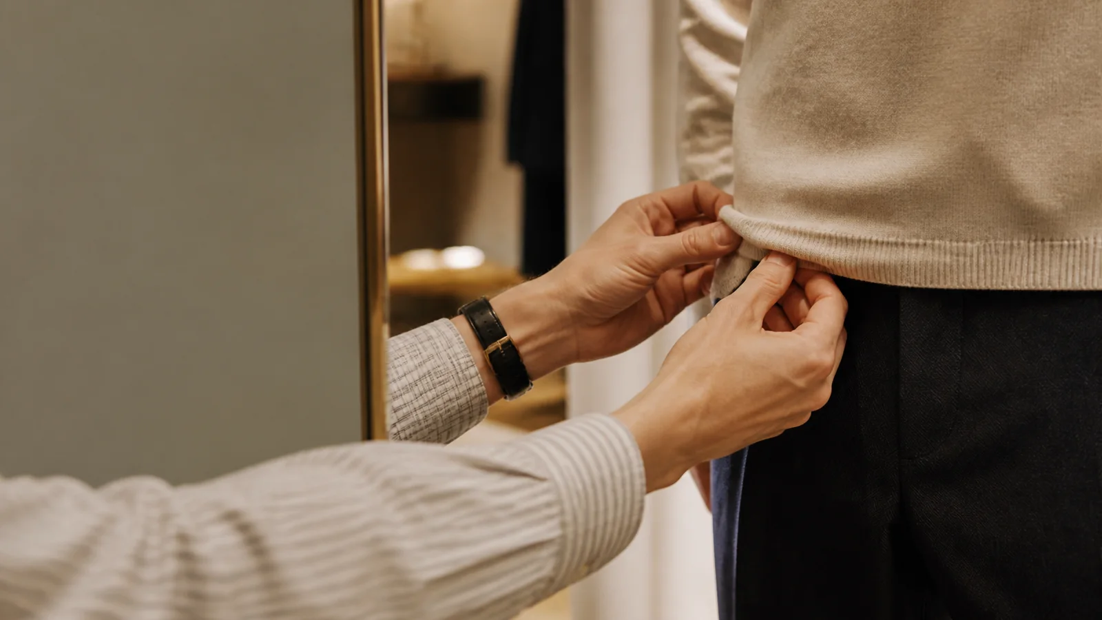 Close-up of hands styling a customer at a fitting mirror, warm interior light, only naturally framed hands, no faces