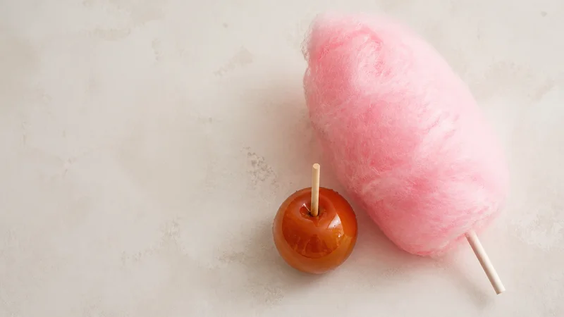 Styled flat-lay of cotton candy and toffee apple on a clean background, soft studio light, generous negative space for overlaid text