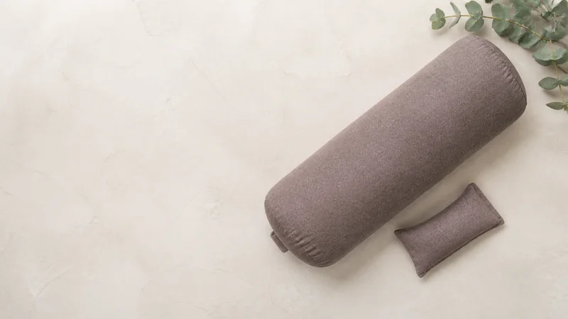Styled flat-lay of a bolster and eye pillow on a clean background, clean even studio light, generous negative space for overlaid text