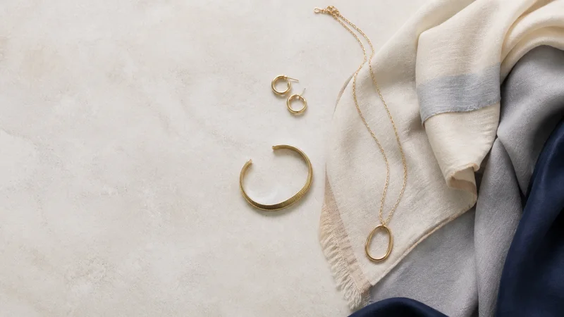 Styled flat-lay of jewellery and scarves on a clean background, clean even studio light, generous negative space for overlaid text