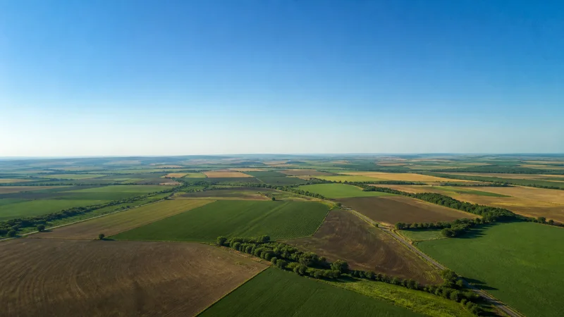 High aerial of a rolling farmland under open sky, a clear blue sky, uncluttered ground and sky bands