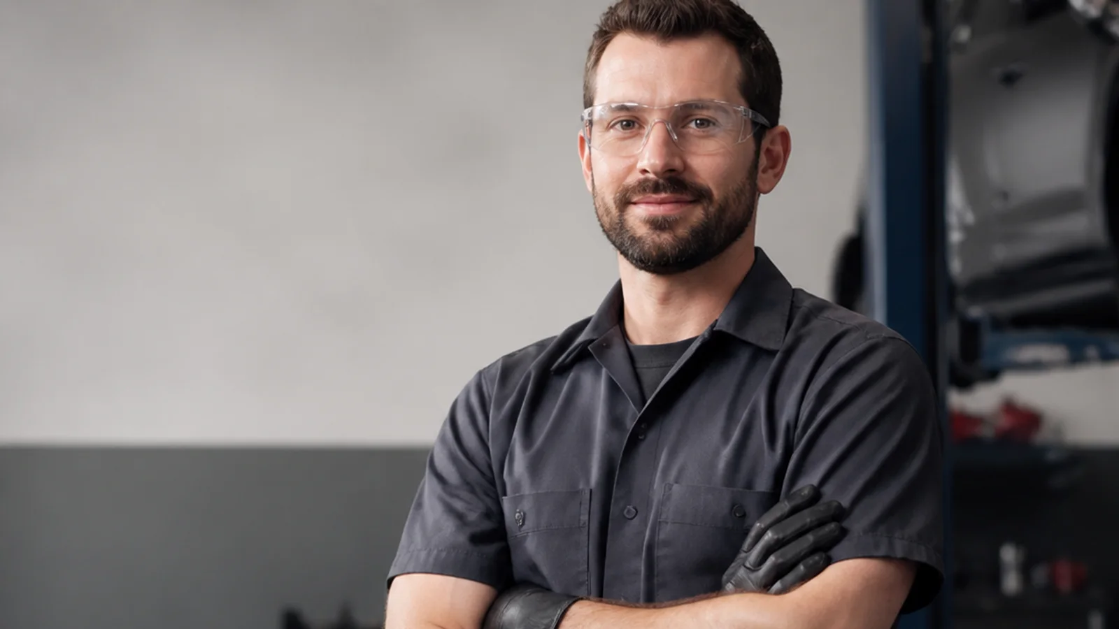 Mid-length portrait of a auto technician, automotive repair, soft even indoor light, plain working backdrop with copy space