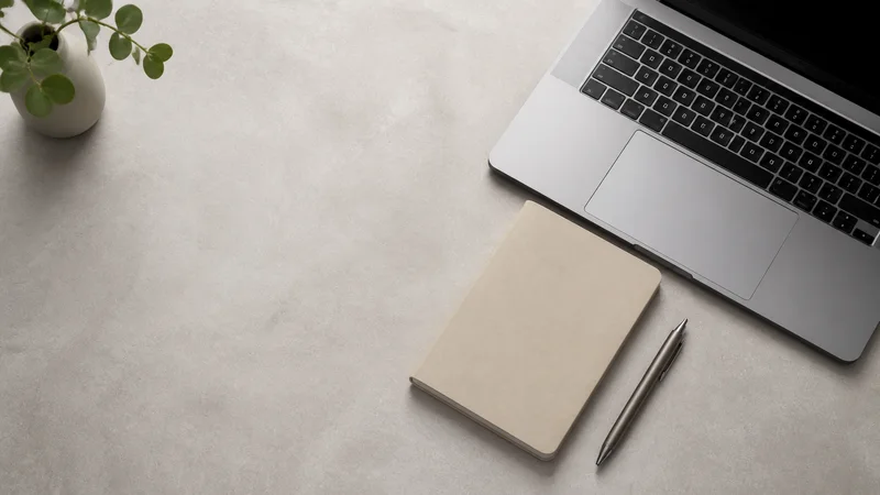 Minimal tidy desk flat-lay with a laptop, notebook and pen, soft studio light, generous negative space