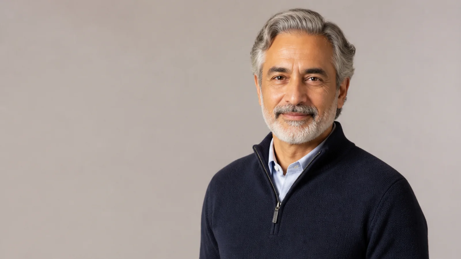 Mid-length portrait of an older adult in smart-casual clothing, plain backdrop with copy space, soft studio light