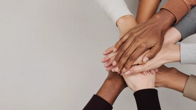 Close-up of diverse hands joined in a teamwork gesture, clean even studio light, no faces