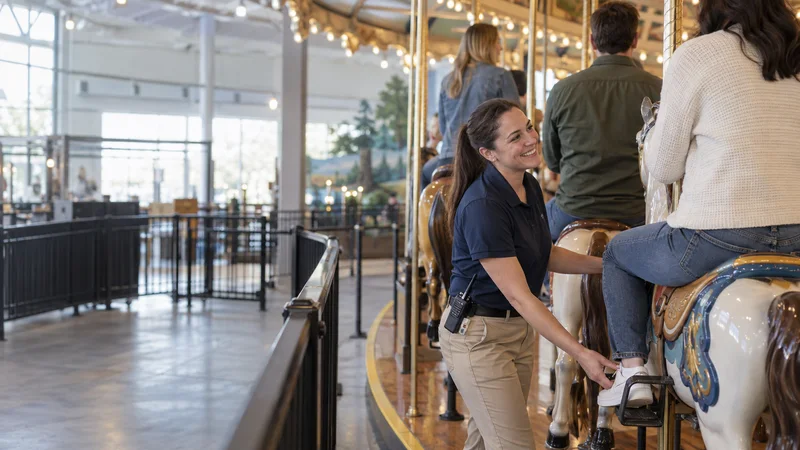 A ride operator loading riders onto the carousel, soft even indoor light