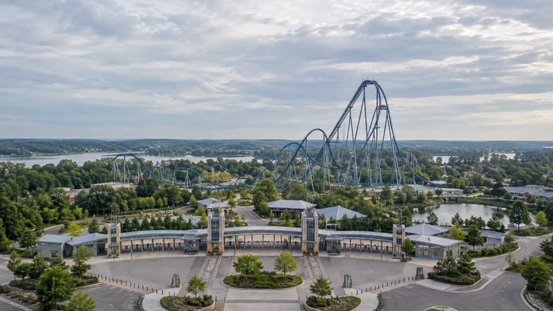 High aerial of a amusement park gates with towering roller coaster, overcast soft light, uncluttered ground and sky bands